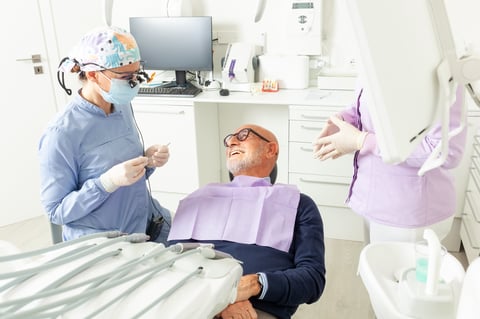 Senior man is lying on dentist chair while dentist is preparing tools for examining his teeth