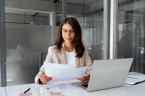 Concentrated latin business woman saleswoman working on laptop computer reading financial bank tax document in office workplace