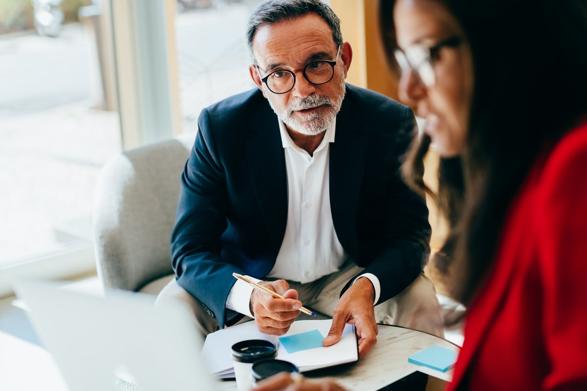 Focused senior manager conversing with a colleague in an office, noting important details during a management planning session.