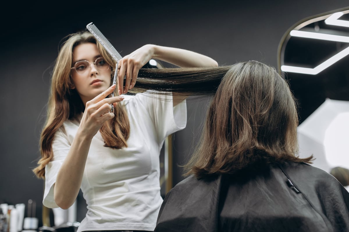 Professional female barber cutting long hair of client in modern barbershop