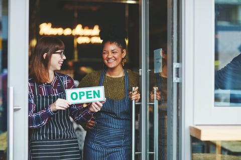 Shot of two young women holding up an open sign in their coffee shop